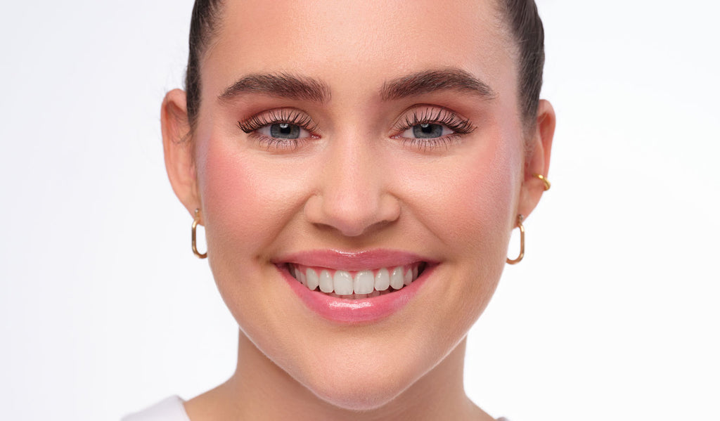 Nachherbild des Clean Girl Make-Up Looks. natürlich geschminktes und lächelndes Model mit strengen Zopf.