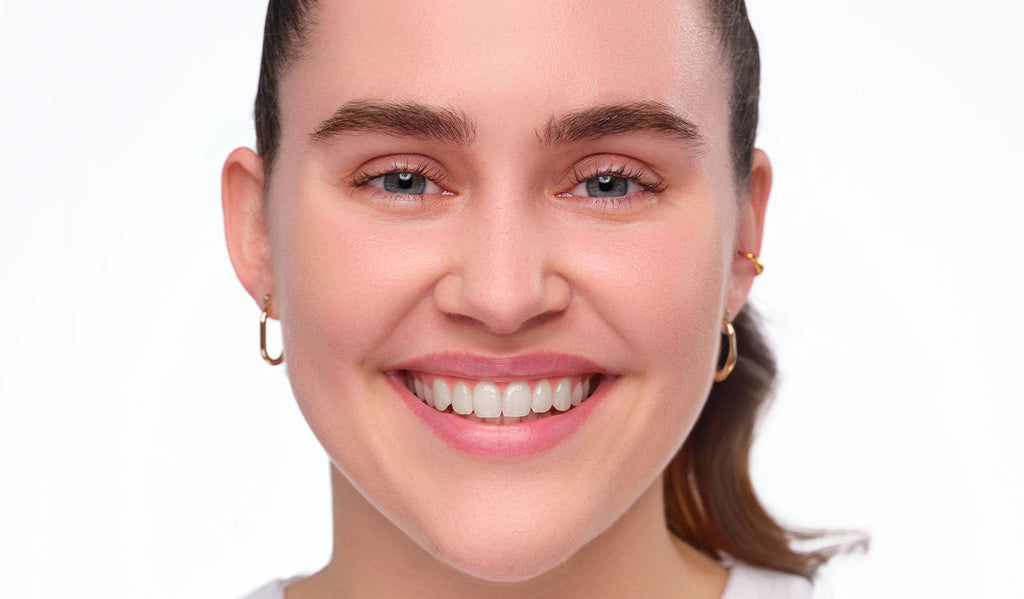 Vorherbild des Clean Girl Make-Up Looks. Ungeschminktes lächelndes Model mit strengen Zopf.