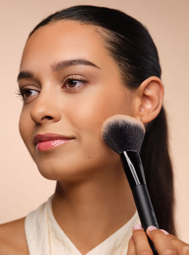 Model trägt Bronzer mit fluffigen Puderpinsel auf