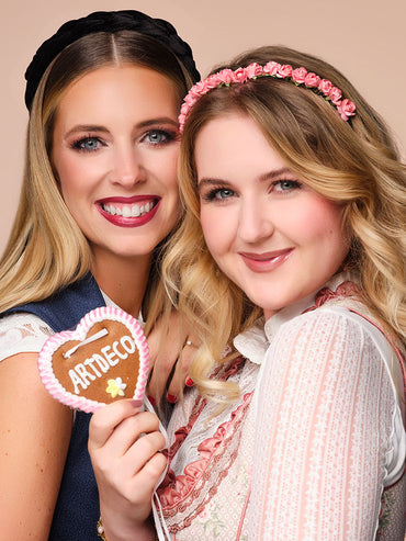 Beide Models mit fertigem Oktoberfest Make-up lachen in die Kamera, es wird ein Lebkuchenherz in der Hand gehalten