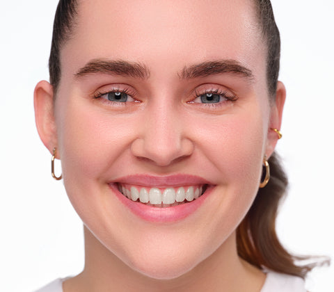 Vorherbild des Clean Girl Make-Up Looks. Ungeschminktes lächelndes Model mit strengen Zopf.