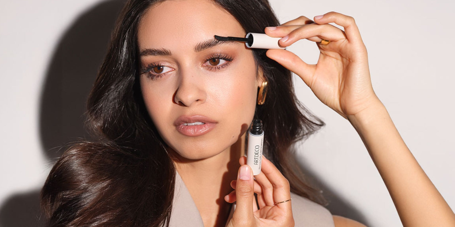 Geschminktes Model hält die Brow Lift Lamination in der Hand und fixiert sich die Augenbrauen mit dem Applikator.