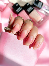 Fertiges Nagel Design des Blush Nail Tutorials mit unscharfen Nagellacken im Hintergrund