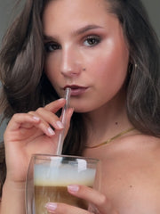 Model mit geschminktem Latte Make-Up trinkt einen passenden Latte Macchiato mit einem Strohhalm.