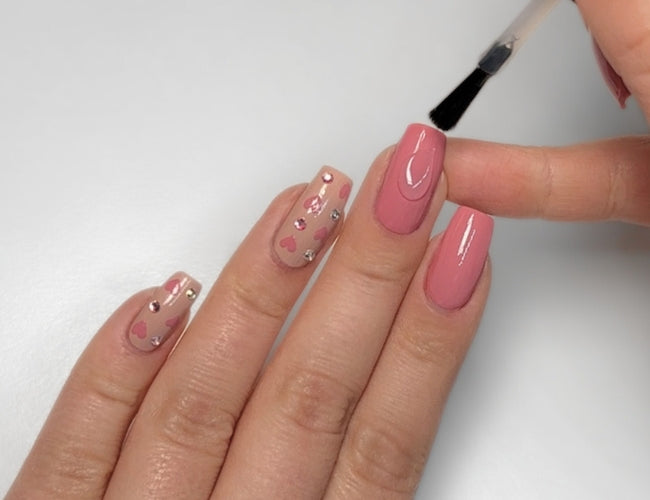 Mit einem Top Coat wird abschließend das Valentinstags Nagel Design versiegelt.