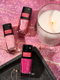 Verschiedene Nagellacke in rosa Tönen und eine passende Kerze liegen auf einem rosa Marmor Hintergrund.