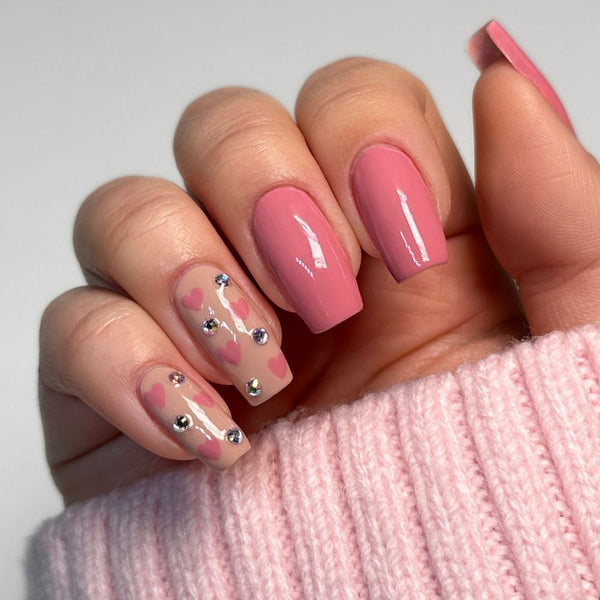 Nageldesign für Valentinstag mit rosa Herzen und glitzernden Steinchen.