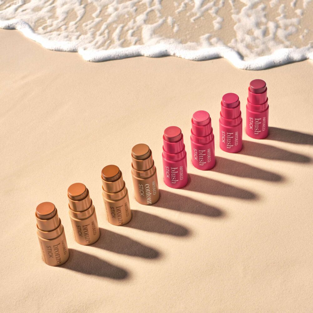 Alle Artdeco Stick Produkte im Sand platziert und mit Wellen im Hintergrund.