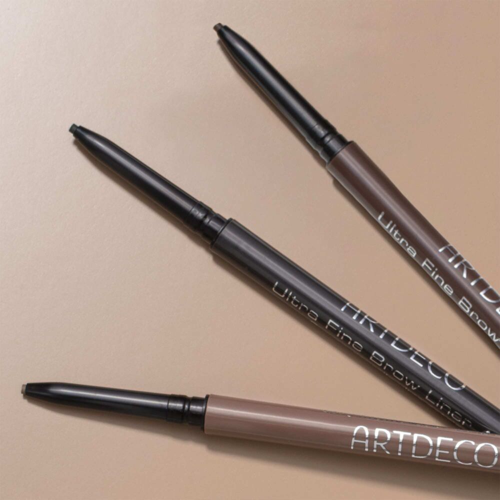Drei Farben des Ultra Fine Brow Liners ohne Kappe auf braunem Hintergund.