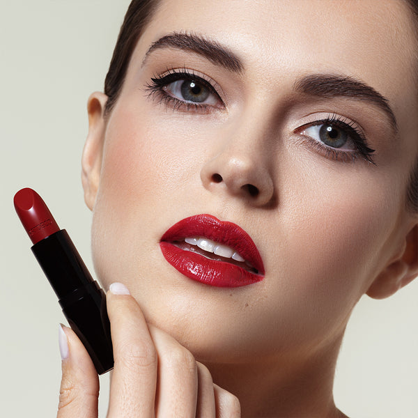 Frau mit leichten Make-up und roten Lippen posiert mit roten Lippenstift in der Hand