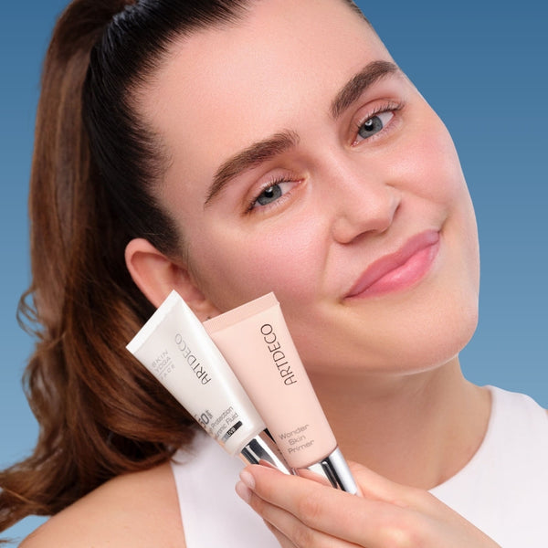 Model mit dezentem Make-Up hält zwei Artdeco Produkte in der Hand, die für eine leichte Sommerpflege geeignet sind. (High Protection Hyaluronic Fluid SPF 50 und Wonder Skin Primer)