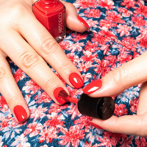 Frau in einem blumigen Kleid trägt farbintensiven roten Nagellack auf 
