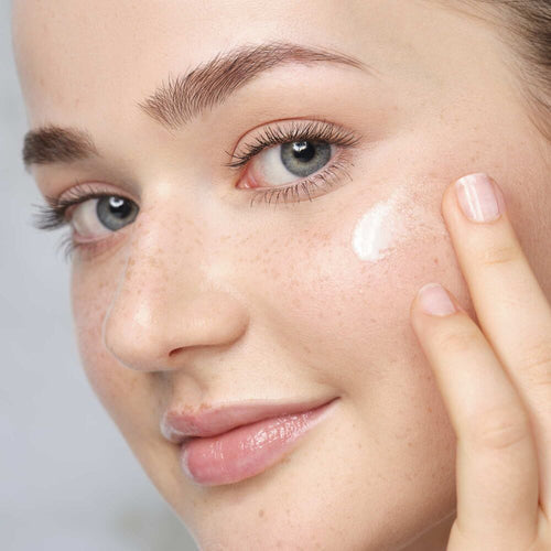 Ein Model trägt etwas Creme auf die Wange auf.