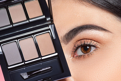 Eine Frau mit geschminkten Augenbrauen wird gezeigt, die eine Augenbrauenpuder Palette vor ihr Gesicht hält