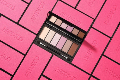 Geöffnete Lidschatten Palette angeordnet zwischen geschlossenen Paletten mit pinkem Design.