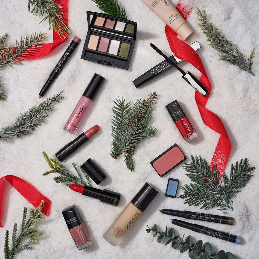 Unterschiedliche Kosmetik Produkte von ARTDECO liegen auf einem Untergrund aus Schnee und sind umgeben von einzelnen Tannenzweigen