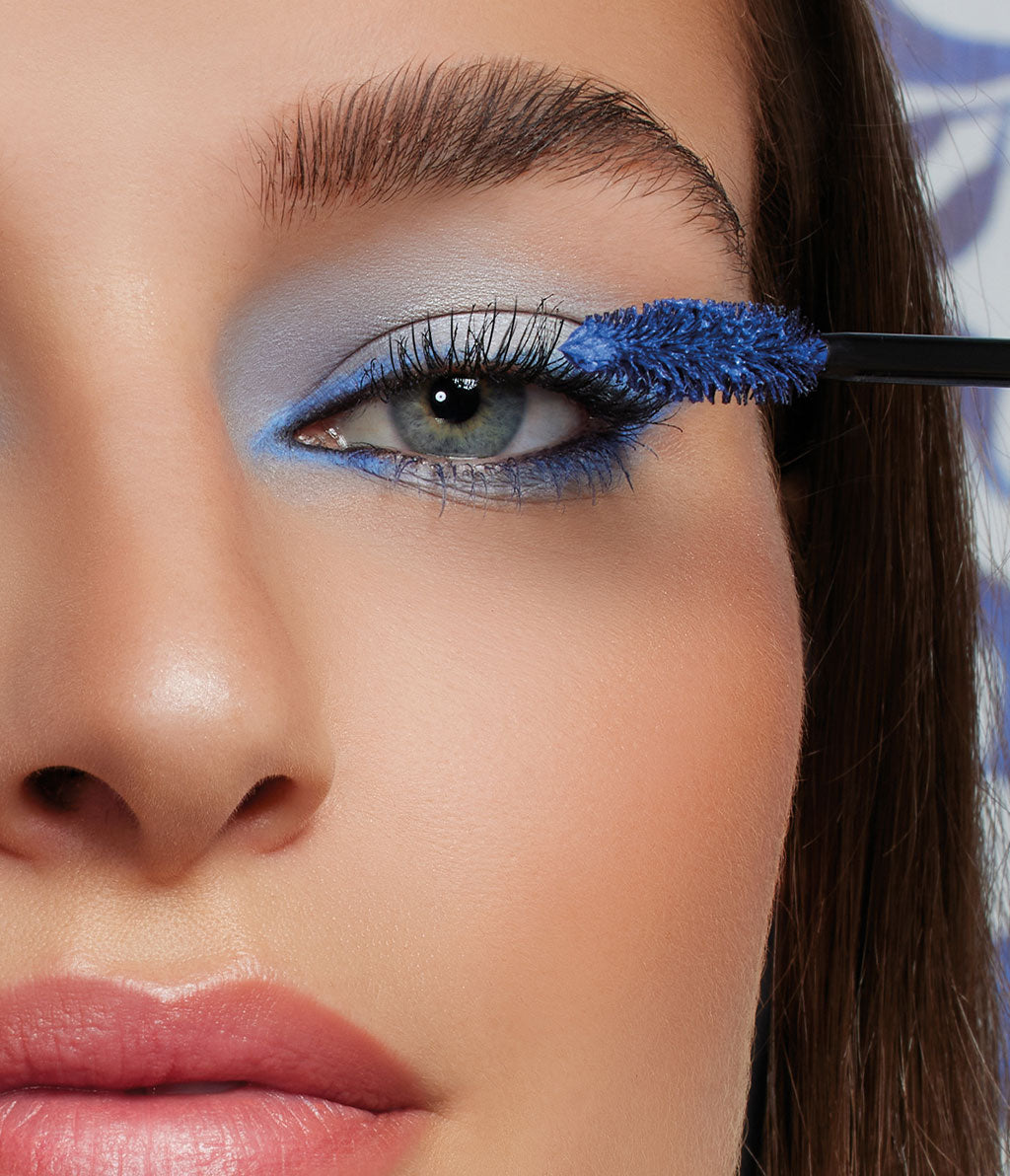 Frau mit langem braunem Haar trägt die neue Volume Sensation Mascara in ocean blue auf die oberen Wimpern auf. Ihr Augen-Make-up besteht ausleuchtend blauem Lidschatten und passendem Eyeliner