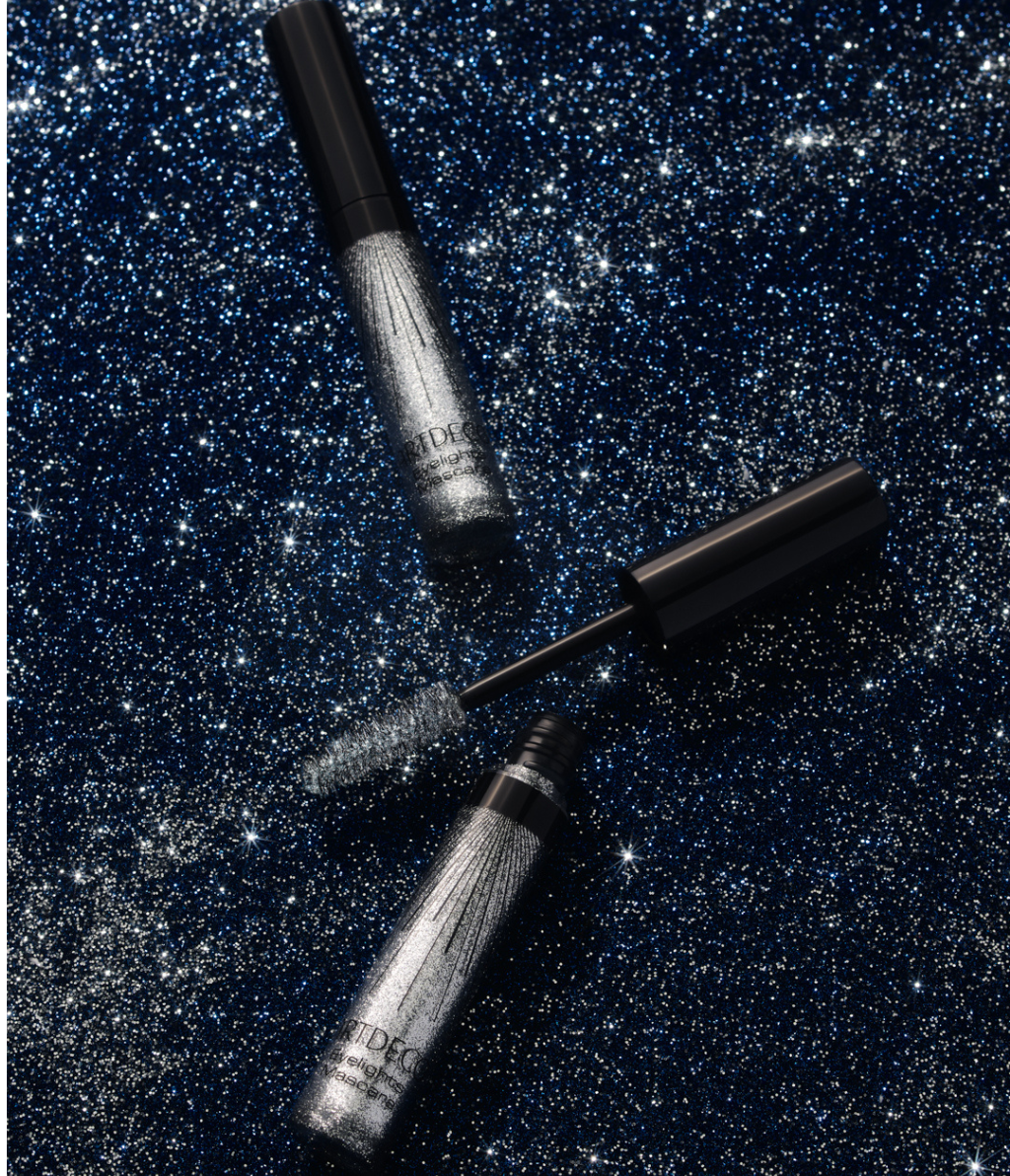 Eine geöffnete und eine geschlossene Eyelights Mascara liegen auf einem blauen Glitzer-Hintergrund.
