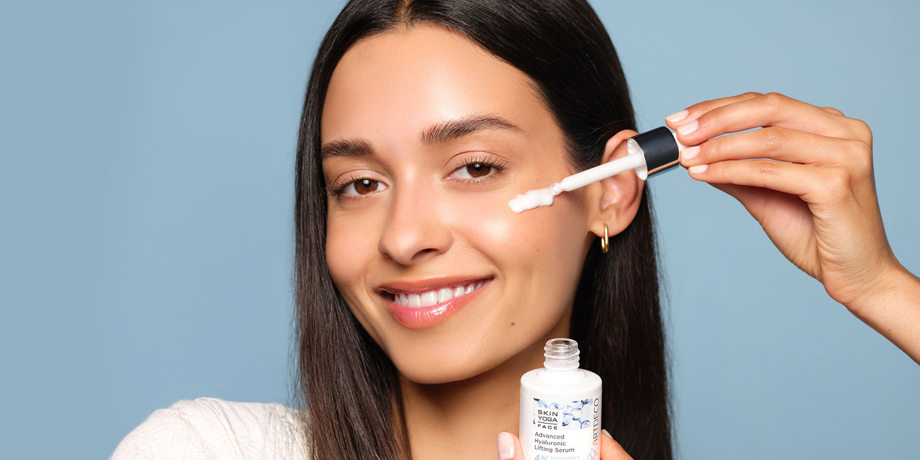 Brünettes Model trägt das Advanaced Hyaluronic Lifting Serum mit einer Pipette auf ihre Wange auf. Das Produkt ist Teil der Super Skin Replump-Pflegelinie mit 3-fachen Hyaluronkomplexen