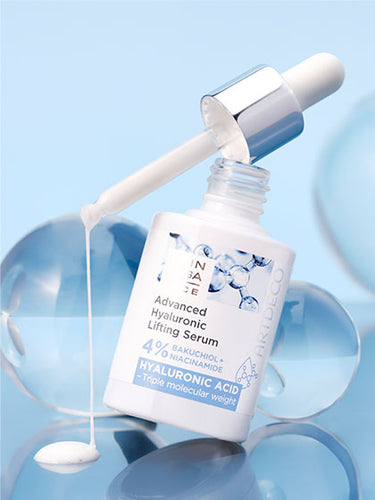 Das Advanced Hyaluronic Lifting Serum vor einem hellblauen Hintegrund umgeben von verschieden großen Glaskugeln.  Aus der Pipette tropft Produkt auf den Untergrund.