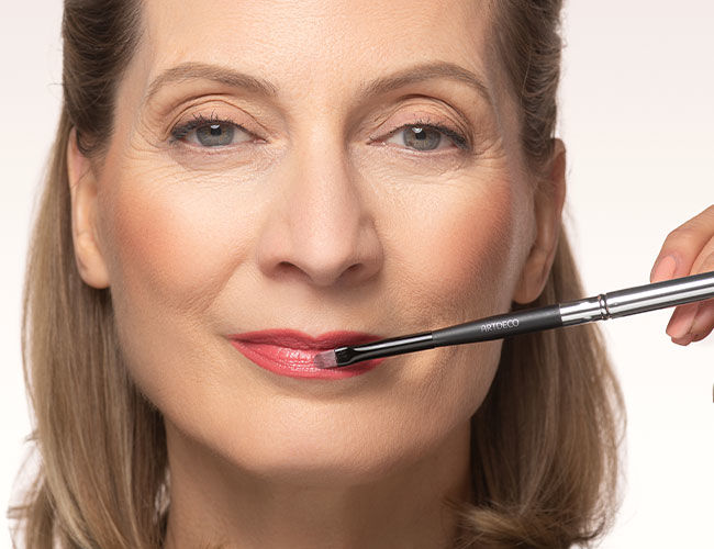 Pinker Lippenstift wird mit einem Pinsel auf die Lippen aufgetragen