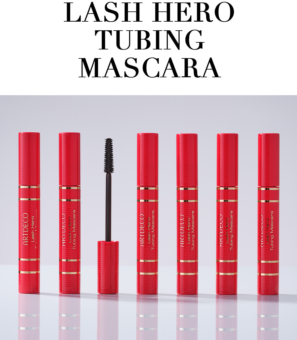 Fünf geschlossene Lash Hero Tubing Masaras im limitierten roten Design Lip stehen geschlossen aufgereiht auf einem neutralen Hintergrund. Außerdem wird zusätzlich das Bürstchen der Mascara gezeigt. Zudem steht in Großbuchstaben der Name des Produktes »Lash Hero Tubing Mascara«.