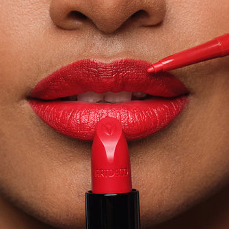 Close-up auf die geschminkten Lippen des Models an welche ein roter Lippenstift und Lipliner gehalten wird
