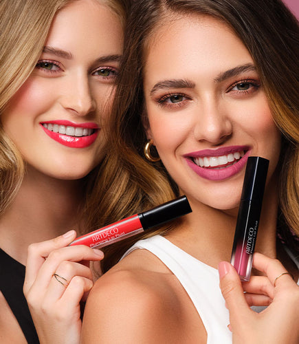 Zwei Frauen halten lächelnd Lippenstiftprodukte in der Hand