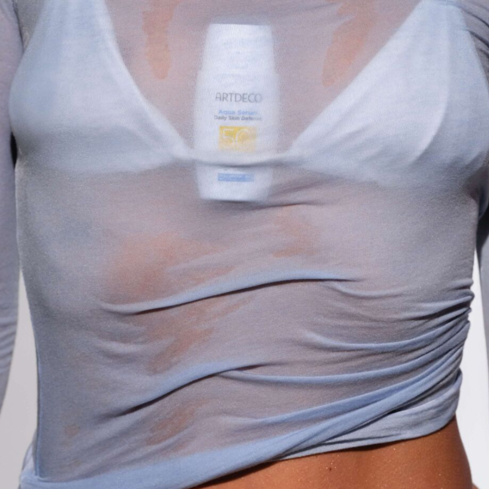 Model hat das Aqua Serum unter ihr Bikini Oberteil geklämmt und trägt ein nasses, leicht durchsichtiges Oberteil darüber