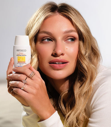 Blondes Model hält das Tinted Aqua Serum Daily Defense SPF50+ in der Hand