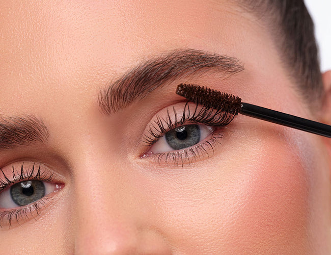 Model trägt die braune ARTDECO All in One Mascara auf die oberen Wimpern auf, um den natürlichen Look des Clean Girl Make-Up zu unterstreichen.