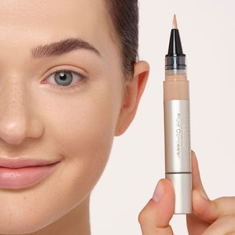 Model hält einen Concealer neben ihren Kopf und lächelt dabei.