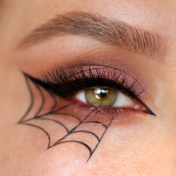 Glamouröses Halloween Make-Up mit schimmerndem Lidschatten, Lidstrich und gezeichnetem Spinnenweben unter dem Auge.