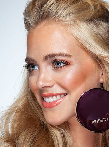 Model mit sommerlichem Make Up Look hält einen kompakten Bronzer neben dem Gesicht