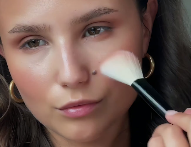 Model trägt roséfarbenes Blush auf die Wangen auf und verleiht dem Latte-Make-up einen frischen Herbst-Touch.