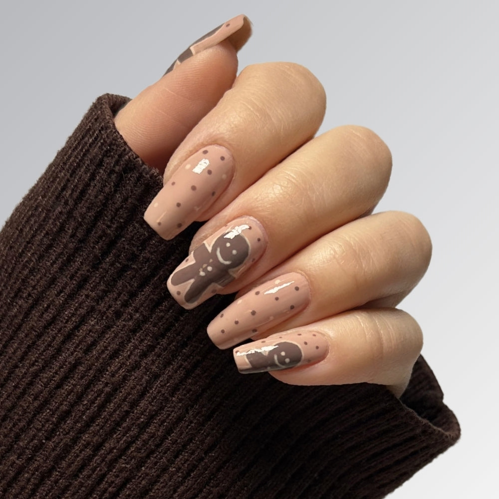 Hand mit weihnachtlichem Nageldesign: Lebkuchenmännchen auf nudefarbenem Hintergrund, verziert mit Punkten, perfekter Winterlook.