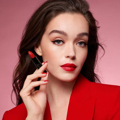 Model mit rotem Lippenstift und passendem Nagellack hält den roten Lippenstift zwischen ihren Fingern.