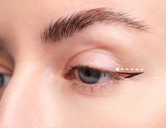 Ein weißer Pfeil zeigt wie man einen klassischen Eyeliner zeichnet.