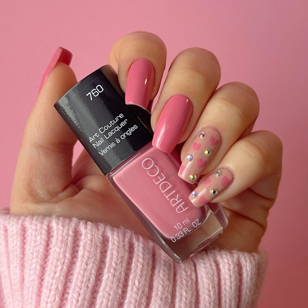 Hand mit fertigem Nagel Design für den Valentinstag. Rosa Herzen und Glitzersteinchen und Art Couture Nail Lacquer Nummer 760.