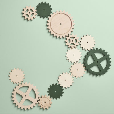 Grüne und holzfarbene Zahnräder, die in einander greifen auf hellgrünem Hintergrund.